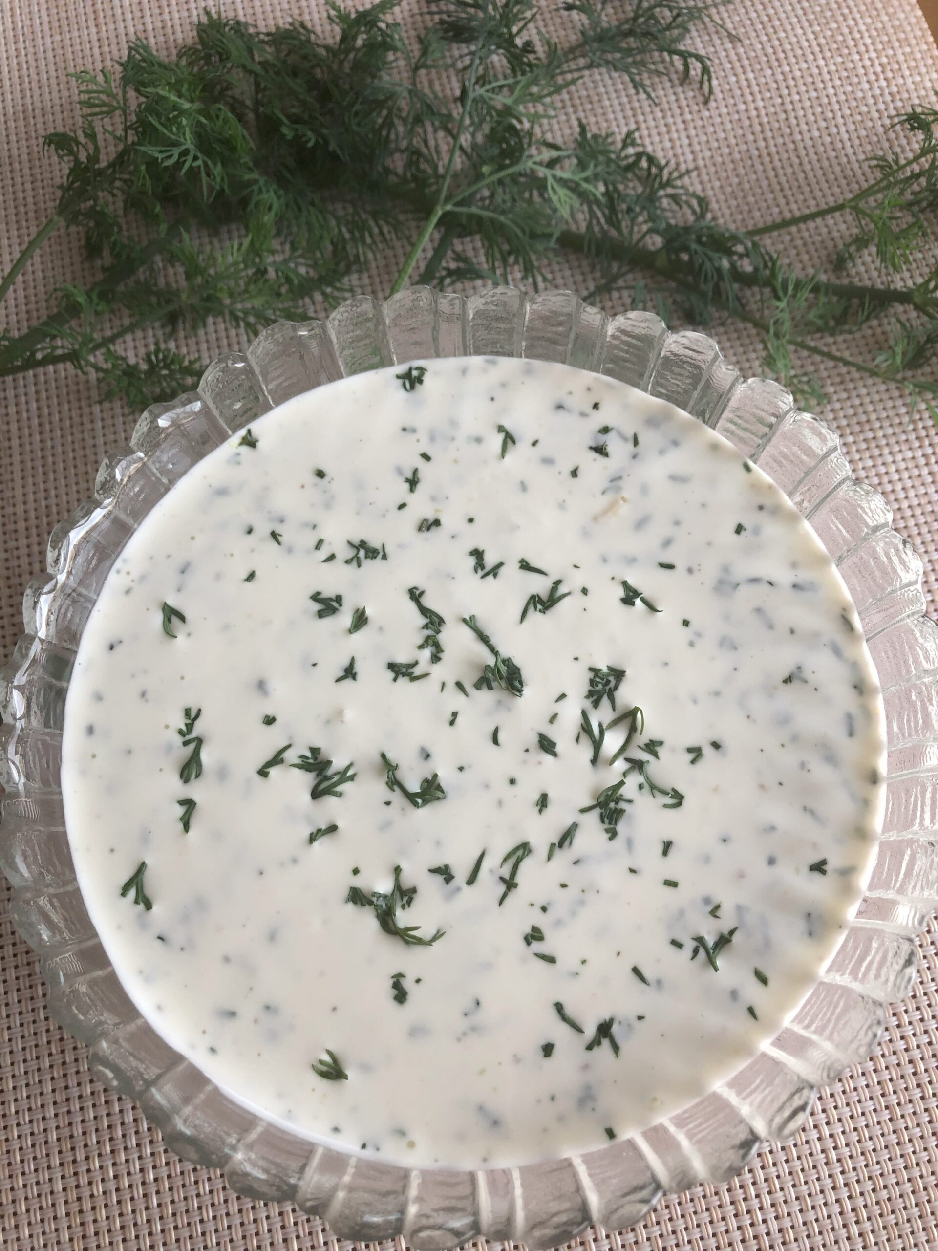 Dill Sauce displayed in the bowl on the table with dill springs next to it.